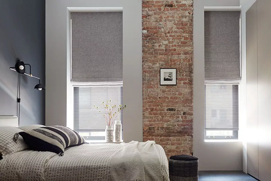 A bedroom with a brick column features inside mount roman shades, showing why you would choose inside vs outside mount blinds