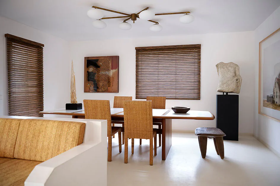 A modern dining room has a tall window with outside mount blinds showing how inside vs outside mount blinds are different