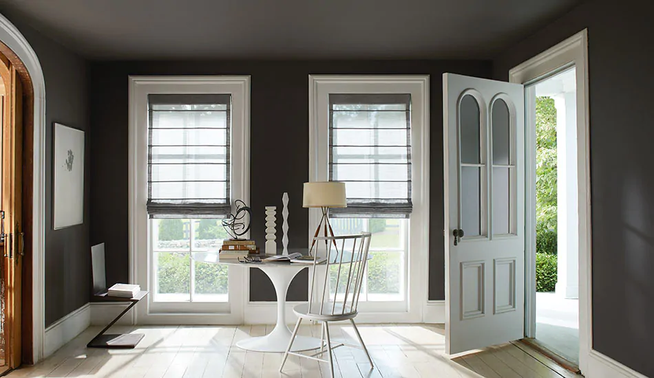 An office with tall windows has Aventura Roman Shades in Sheer Wool Blend, Urban Grey, showing one type of roman shade styles