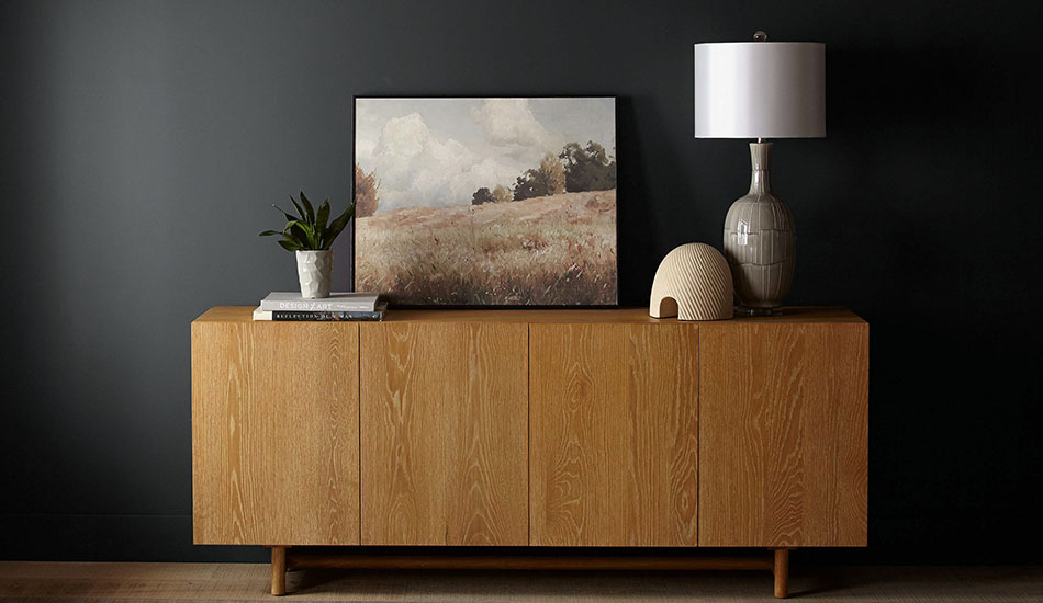 A credenza made of honey colored wood sits in front of a wall painted in Behr's color of the year 2024, Cracked Pepper