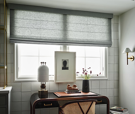 Roman Shades for kitchen windows include Cascade Roman Shades made of a grey texture fabric above a desk in a kitchen alcove