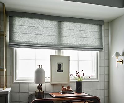 Cascade linen Roman Shades made of C.O.M. material in a light grey filter light onto a small office desk