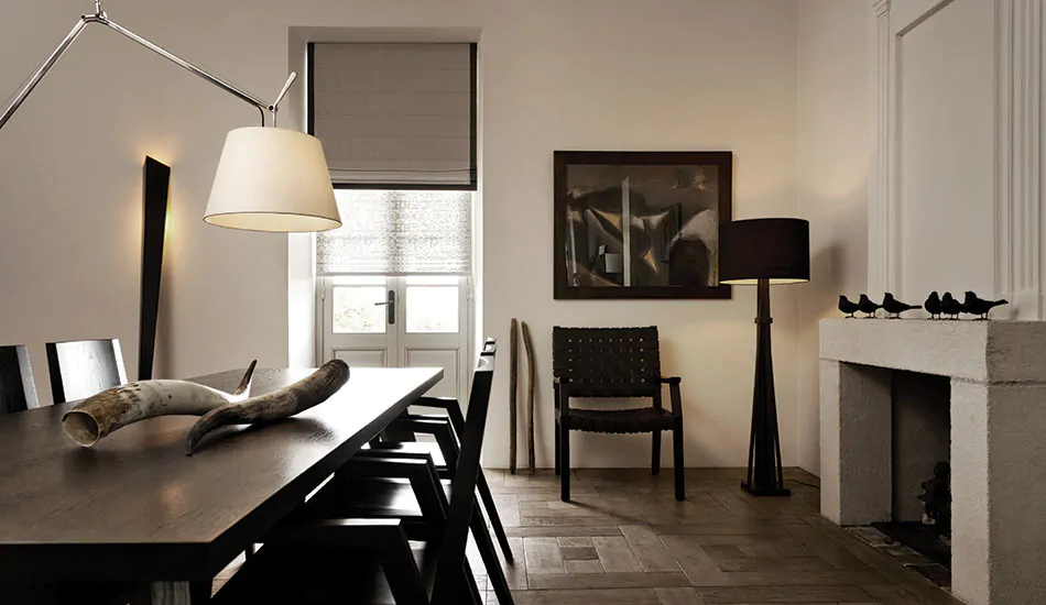 A rustic, mid-century modern dining room features a french door covered by a Cascade Roman Shade made of Linen Blend in Ash