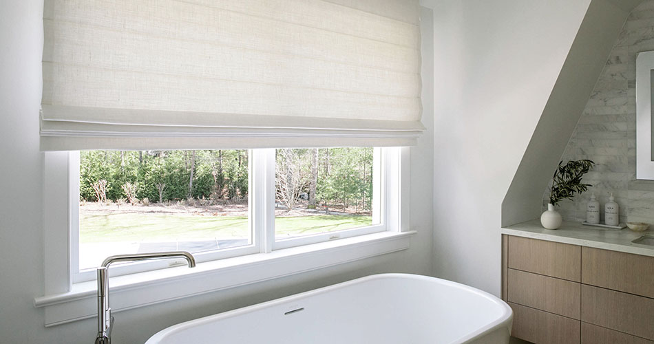 A simple white bathroom features a Cascade Roman Shade made of Luxe Linen in Optic White with motorized lift