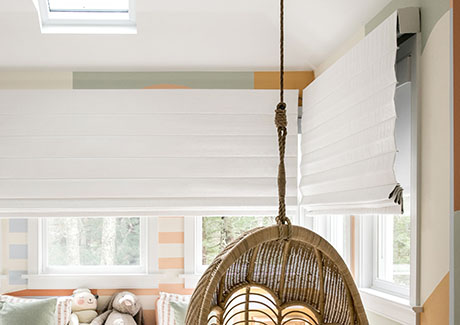 A kids room features Cascade Roman Shades made of Luxe Linen in Optic White layered with Roller Shades made of Flock in White