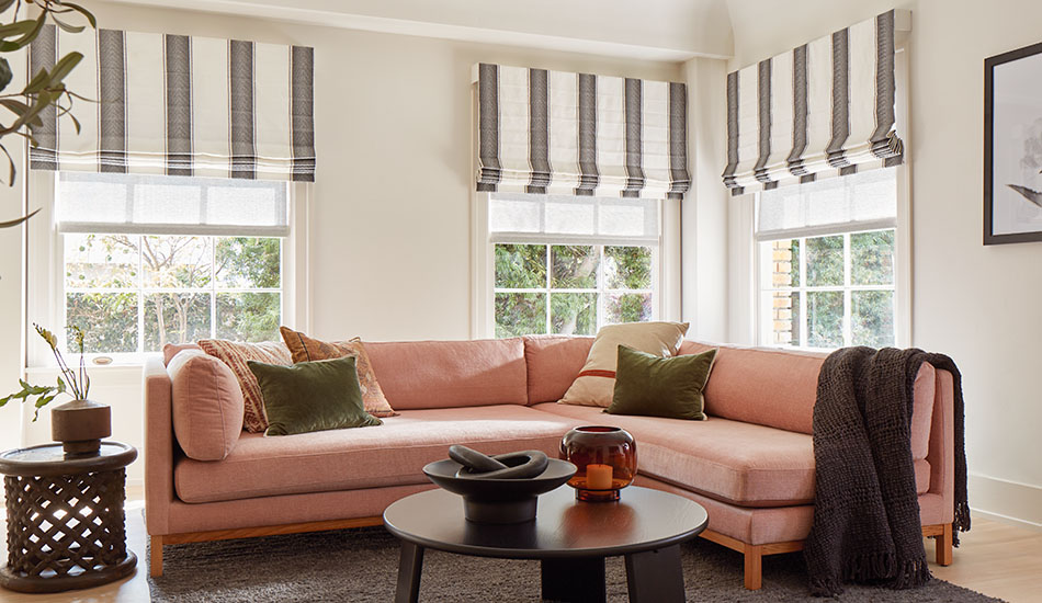 A family room with a peach sofa has Cascade Roman Shades in Nomad Stripe, Granite, showing one type of roman shade styles