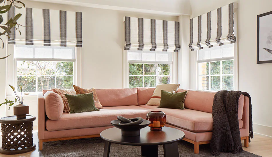A family room with a peach sofa has Cascade Roman Shades in Nomad Stripe, Granite, showing one type of roman shade styles