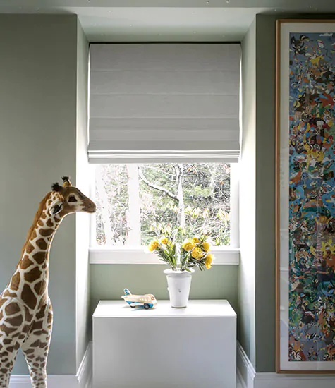 A room with a plush giraffe has blackout shades for nursery windows made of Cascade Roman Shades in Luxe Linen, Optic White