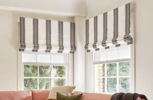 Roman shades for windows include Cascade Roman Shades made of Nomad Stripe in Graphite in a living room with a salmon couch