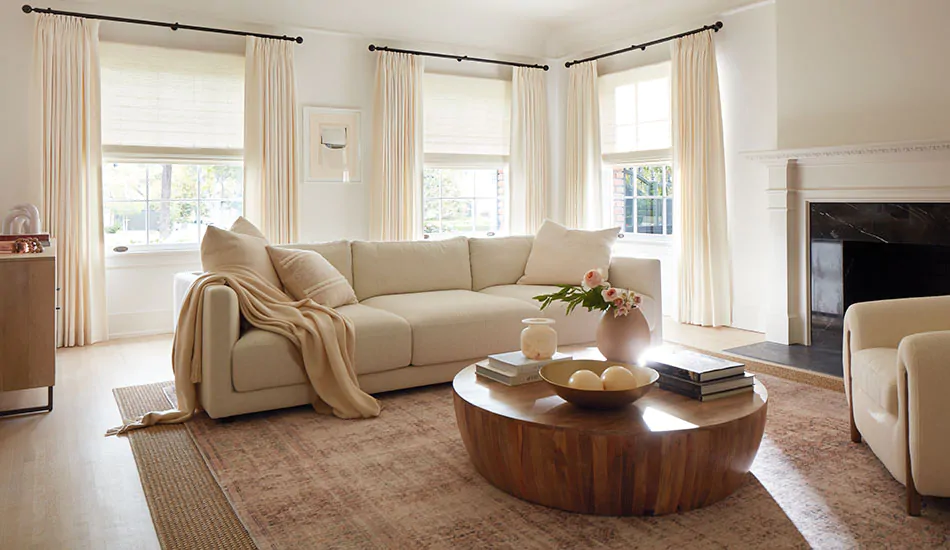 An inviting room has Tailored Pleat Drapery of Luxe Linen in Oyster layered with Woven Wood Shades of Harper in Ivory