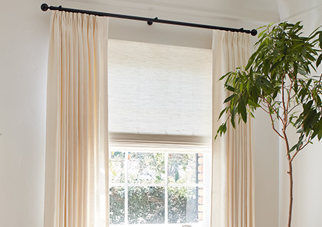 A living room has privacy shades in a Woven Wood Shade style made of Harper in Ivory with privacy lining as natural window coverings that balance light and privacy