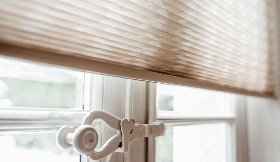 A close up of a French door with an old latch shows the bottom bar of the Cellular Shade made of Campbell in Beige