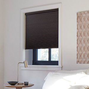 A cellular Shade made of 3-4 Single Cell Blackout in Midnight contrasts the white walls and light wood accents of a bedroom
