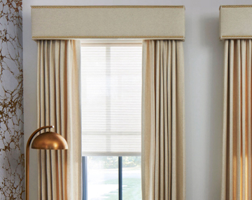 Cornices with Nailheads featured over matching Drapery hung over windows in a room with a marble wall and a gold lamp.