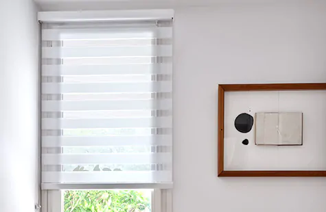 A bedroom with wood tones and décor features Zebra Blinds made of Cataline material in White to match the white walls