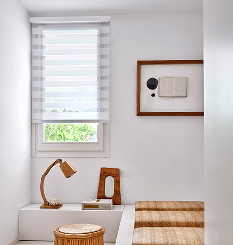 Double Roller Shades made of Catalina in White blend in with the white walls of a bedroom with wood accents