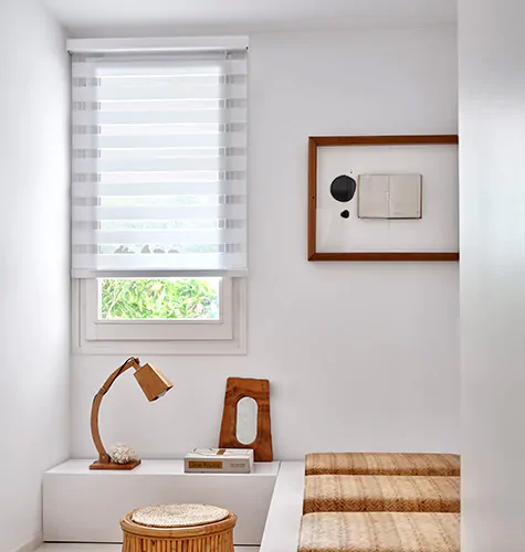 Double Roller Shades made of Catalina in White blend in with the white walls of a bedroom with wood accents