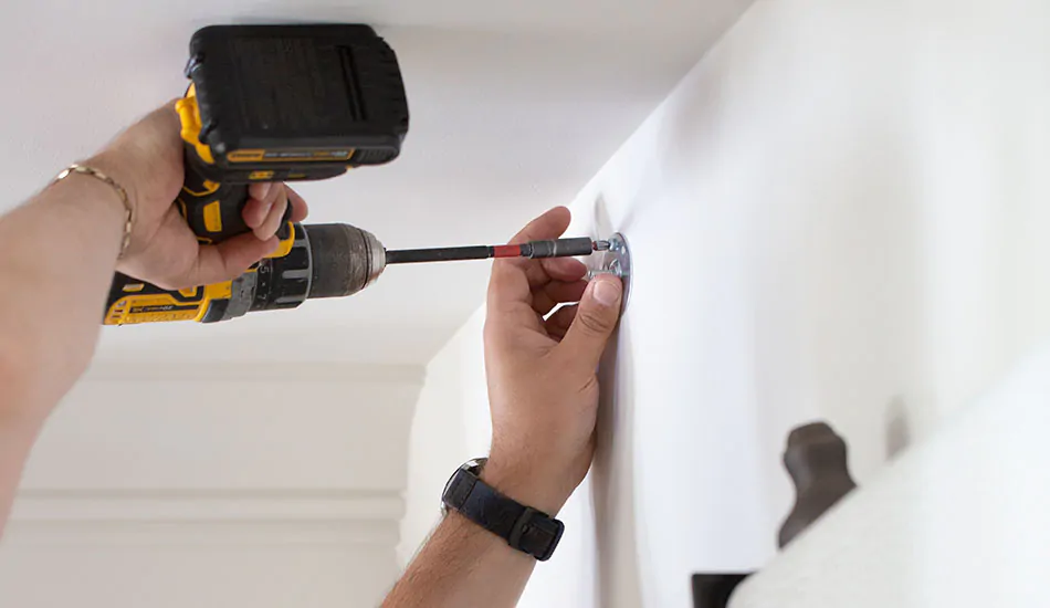 A close up shows a professional with a drill and bracket showing how to install curtain rod brackets