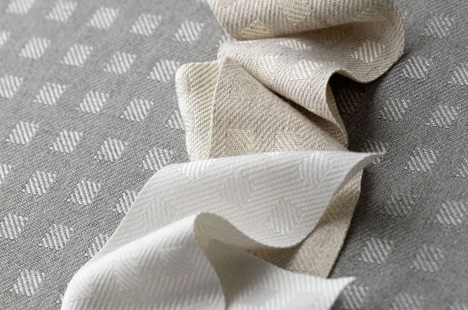 A close-up shot of material swatches for plaid curtains in Osprey Check in Cloud, Parchment and Nickel colors