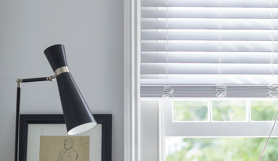 Faux Wood Blinds in Blanc hang partially down a window in a white room showing how to lower blinds halfway