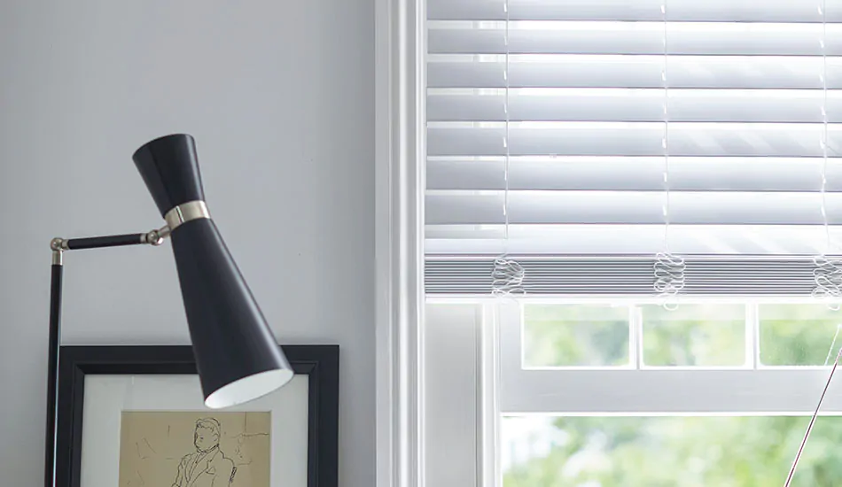 Faux Wood Blinds in Blanc hang partially down a window in a white room showing how to put blinds down halfway