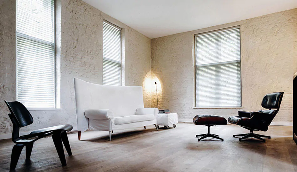 A modern living room with faux wood blinds in Blanc shows what is faux wood as a window treatment