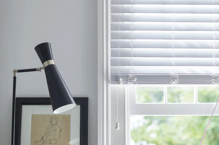 An image to answer what is faux wood shows 2-inch Faux Wood Blinds in Blanc next to white walls and black decor