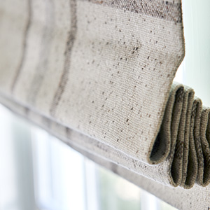 A close up of a Flat Roman Shade made of Aberdeen in Oat shows the texture of the material and stack of the shade