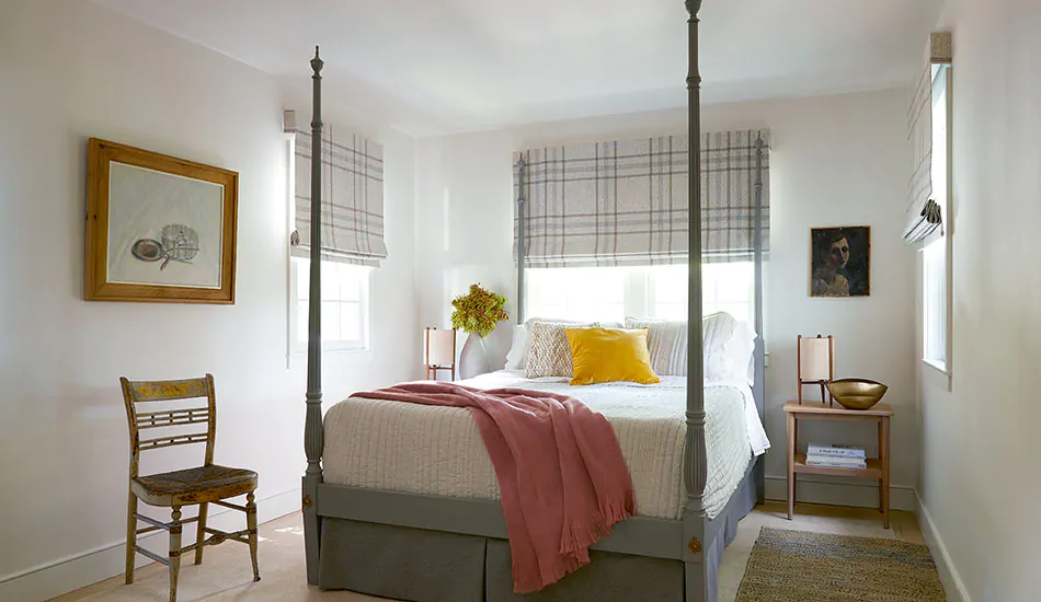 A colonial-inspired bedroom features farmhouse window treatments of Flat Roman Shades made of Aberdeen in Oat