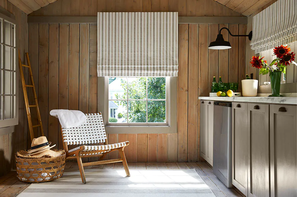Farmhouse window treatments of flat Roman Shades made of Awning Stripe in Fawn adorn the windows of a modern rustic shed