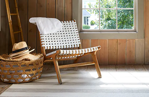 A small room with a wood chair with a woven backing and seat features wood flooring and a bright striped area rug