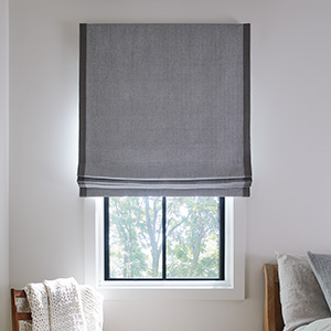 A Flat Roman Shade made of Baldwin in Stone with Flanders trim in Granite adds definition to a bedroom window