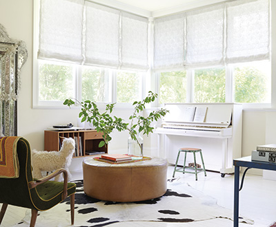 A mid-century modern sitting room has corner windows with Flat Roman Shades made of Feather Palm Embroidery in Vintage Lace