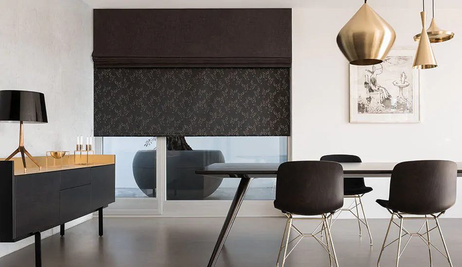 A modern dining room has a dark Roman Shade made of Hemp in Dune layered with a Roller Shade made of Cherry Blossom in Taupe