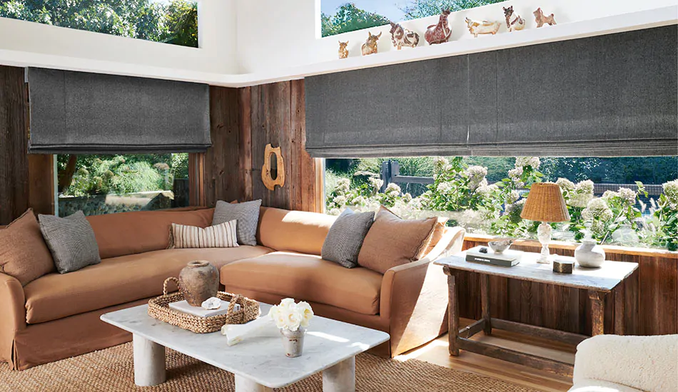 A living room with an earthy color palette features outside mount Roman Shades made of Lowell Tweed in Flint