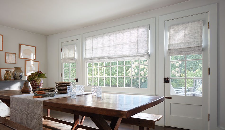 A bright rustic dining room with a dark wood table has Flat Roman Shades made of Shoreline in Cloud for a light inviting look