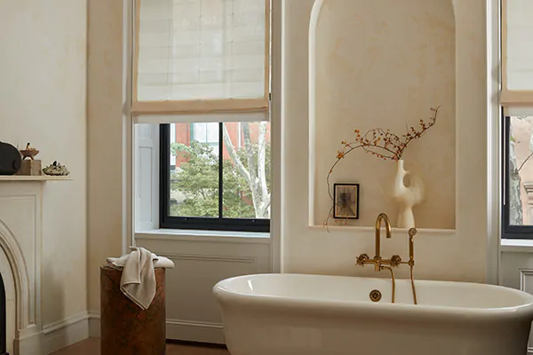 A luxe neutral-toned bathroom with classical decor features a Flat Roman Shade made of Sunbrella Vitela in Ivory