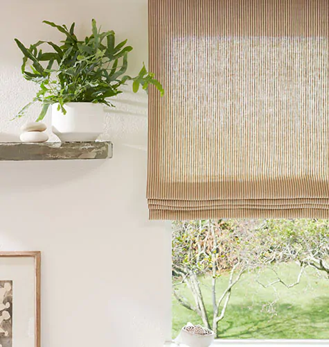 A close up of a Flat Roman Shade made of Surrey Stripe in Morel and Natural is next to a wood shelf with plants