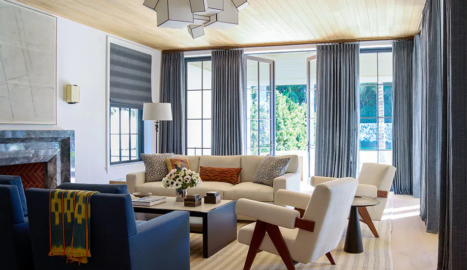 A modern living room with a bold blue couch has Black Roman Shades and Tailored Pleat Drapery made of Jasmine in Midnight