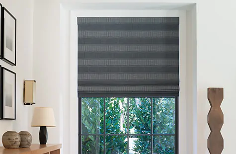 A Flat Roman Shade made of Victoria Hagain's Jasmine in Midnight covers a window in a contemporary room with interesting art