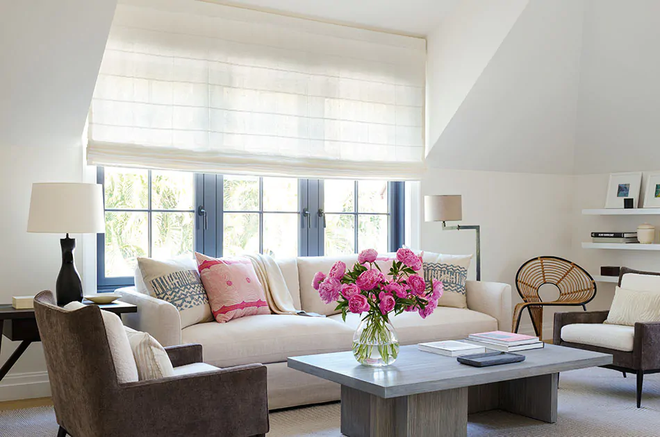 A sunny area with neutral colors and pink flowers with roman shade styles, Flat Roman Shades made of Sankaty Stripe in Moon