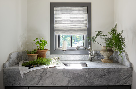 A utility room with a small window has Flat Roman Shade made of Tidal Line in Slate that complements the marble countertop