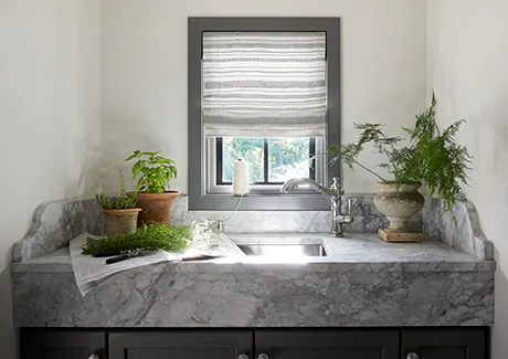 A laundry room features a window above the sink with a Flat Roman Shade made of Tidal Line in Slate for visual interest