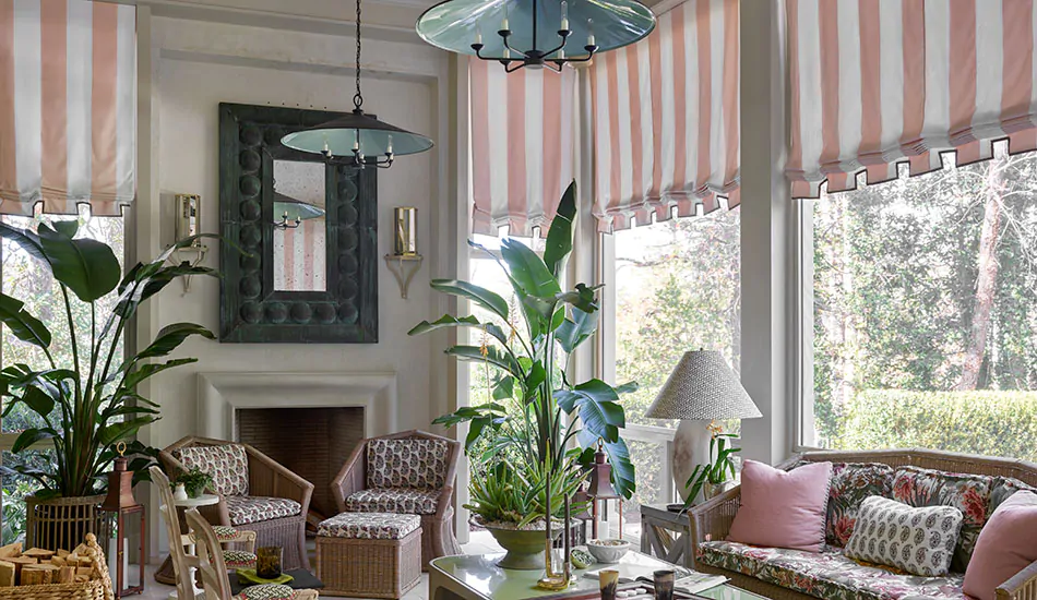 Flat Roman Shades with pink and white stripes are sunroom window treatments in a sunroom with plants and outdoor furniture