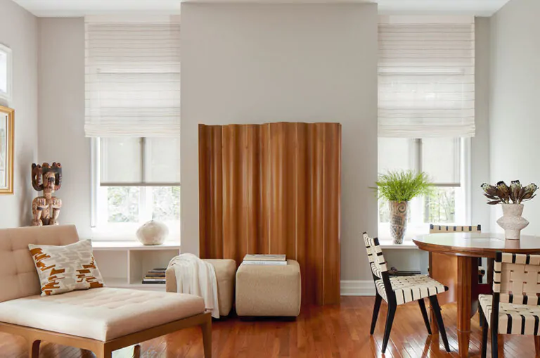 A living room with warm wood tones features outside mount Roman Shades made of Sahara Stripe in Desert for subtle texture