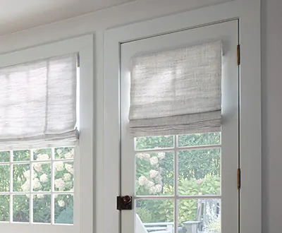 A door window shade is made of a Flat Roman Shade in Shoreline, Cloud and covers part of a door with a latch handle