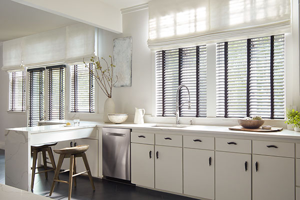 Wood Blinds made of 2-inch Painted Bamboo in Coal contrast the white cabinets and Tangier Weave in Blanco Flat Roman Shades