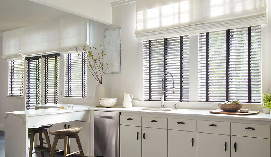 A bright kitchen has Wood Blinds of Painted Bamboo in Coal to contrast light filtering Roman Shades in Tangier Weave, Blanco