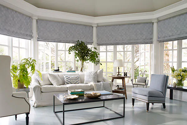 Flat Roman Shades made of Oceana in Slate are used as sunroom window treatments on a bow window and classical details