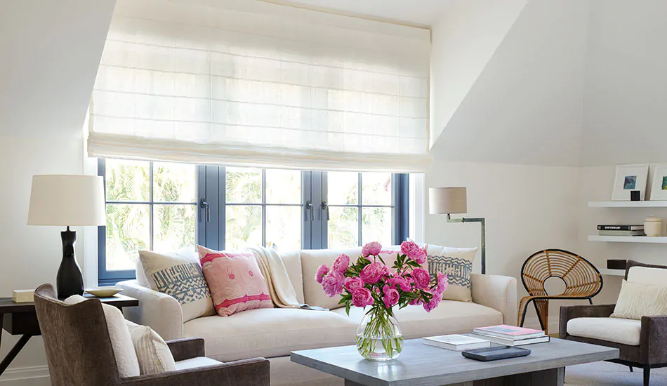 A sitting room with bright pink flowers has privacy shades in the Flat Roman Shade style made of Sankaty Stripe in Moon